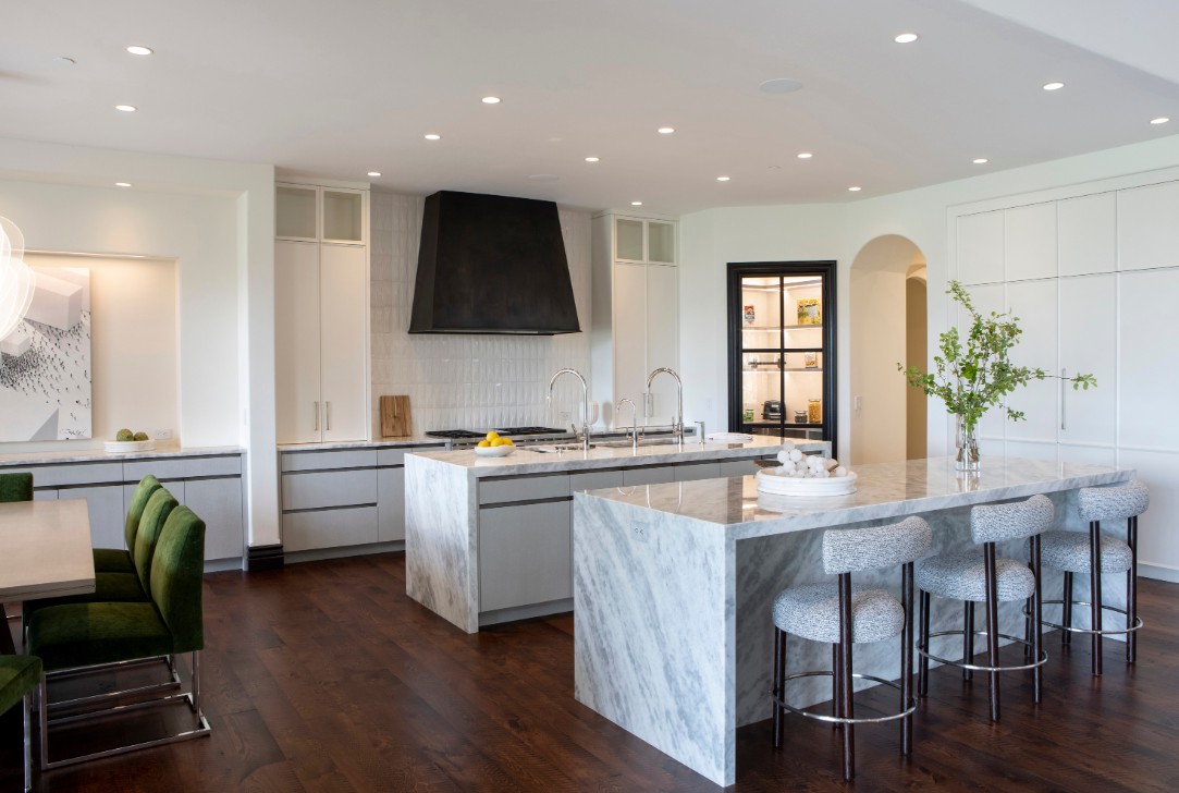 Spacious modern kitchen featuring custom green velvet chairs, double marble islands, and curated lighting for a bespoke interior.