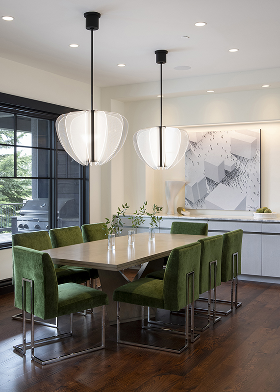 Modern dining room featuring bold green velvet chairs, a light wood table, sculptural twin pendant lights, and a large abstract artwork, showcasing a personal design fingerprint through custom color choices and curated decor.