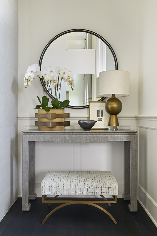 Refined entryway vignette with round mirror, console table, and orchid centerpiece enhancing natural light and symmetry