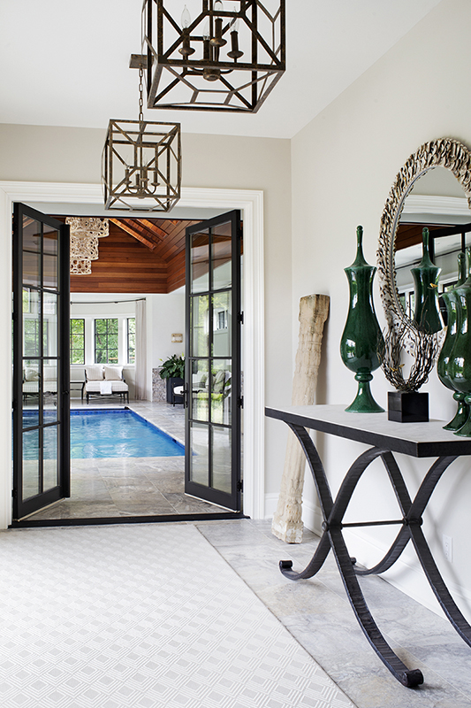 Elegant indoor pool entrance with round mirror and green décor creating a spa-like transitional space