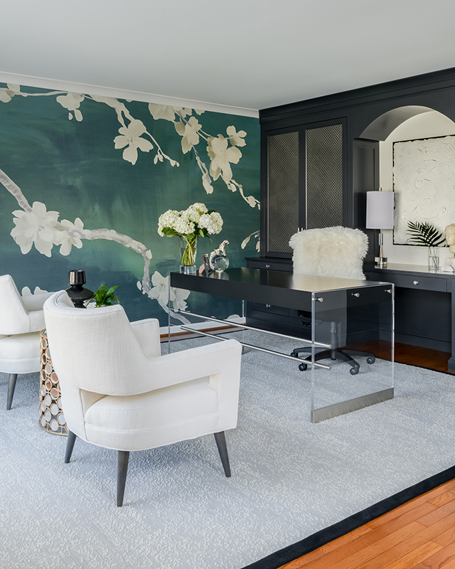 Modern home office with acrylic desk, black built-in cabinets, and statement green floral wall mural.