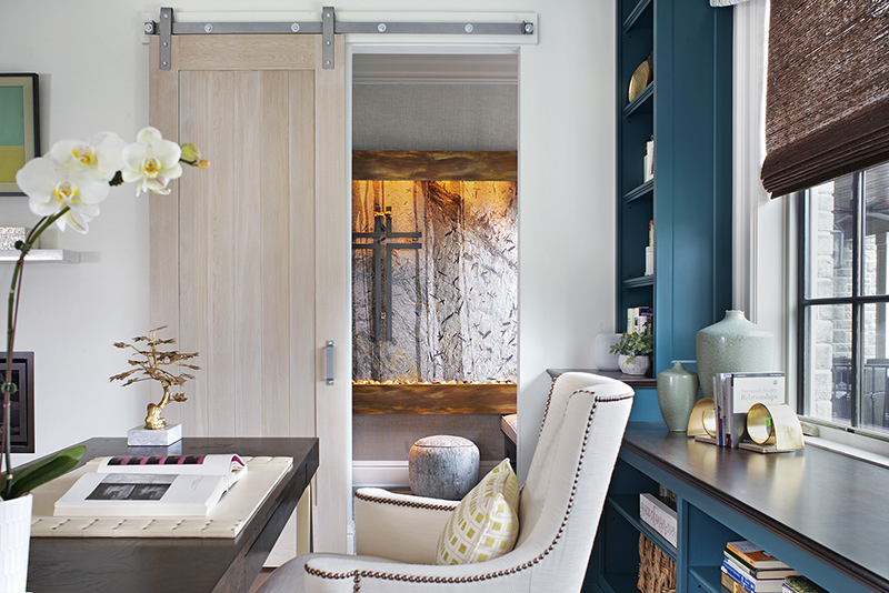 Elegant home office with teal built-in shelves, sliding barn door, and cozy reading nook.