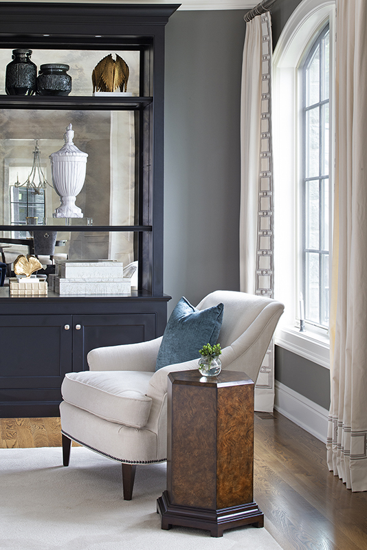 Cozy reading nook with cream armchair, dark cabinetry, and natural light balancing light and dark tones in interior design.