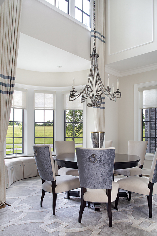 Intimate round dining nook with velvet chairs, handcrafted chandelier, and turret window seating designed by Impeccably Designed Homes.