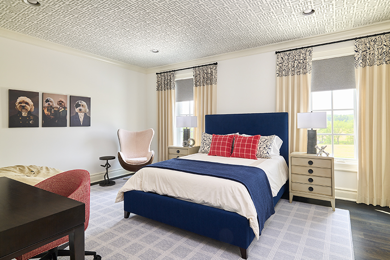 Tween boy bedroom with blue upholstered bed, geometric ceiling wallpaper, and stylish decor – interior design for kids’ spaces by Impeccably Designed Homes.