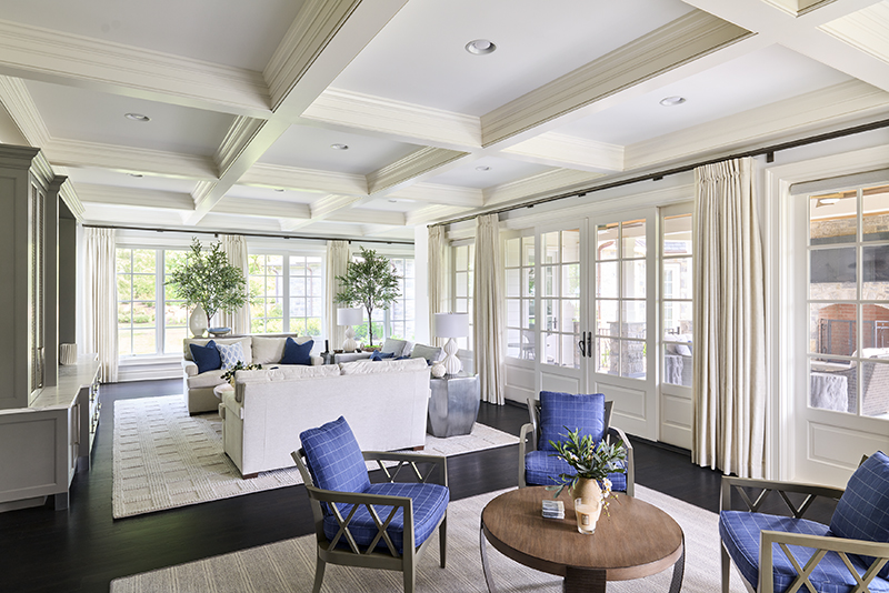 Layered neutrals in interior design featuring a bright living room with cream upholstery, blue chairs, coffered ceiling, and expansive windows