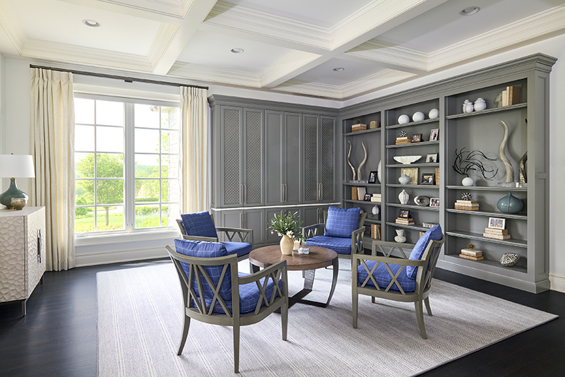 How to design a nurturing space with neutral tones shown through a gray built in bookcase, blue accent chairs, and a soft neutral rug